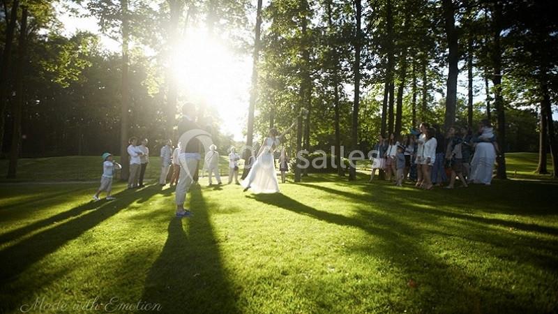 Un groupe de personnes rassemblé dans un parc ensoleillé, entouré d'arbres, avec des ombres longues sur l'herbe.