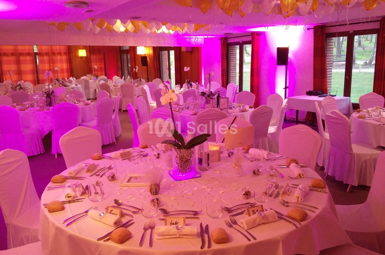 Salle de réception décorée avec des ballons jaunes et blancs, tables rondes dressées avec nappes blanches et orchidées.