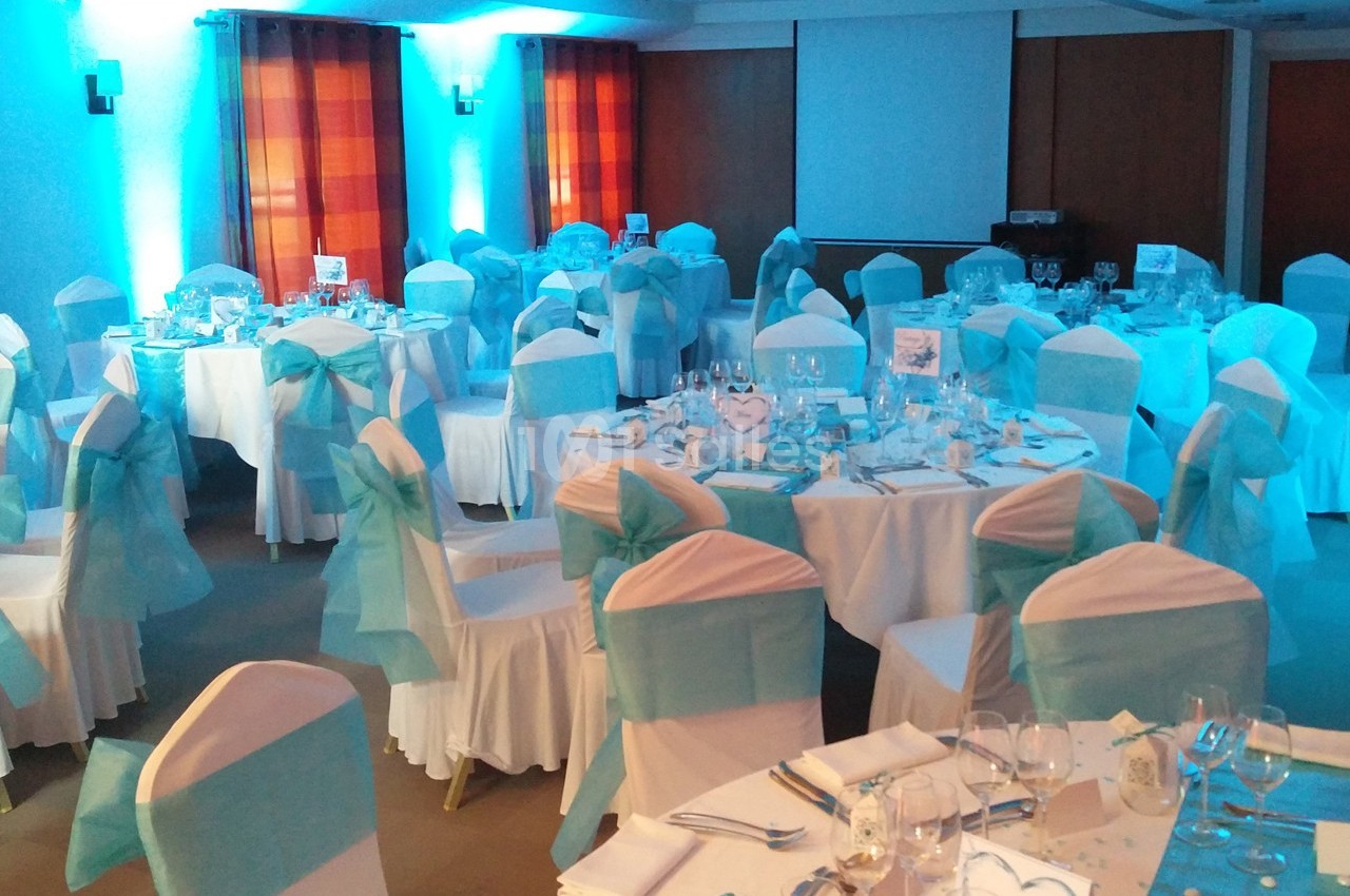 Salle de réception décorée avec des nappes blanches et des nœuds turquoise sur les chaises, tables dressées pour un…