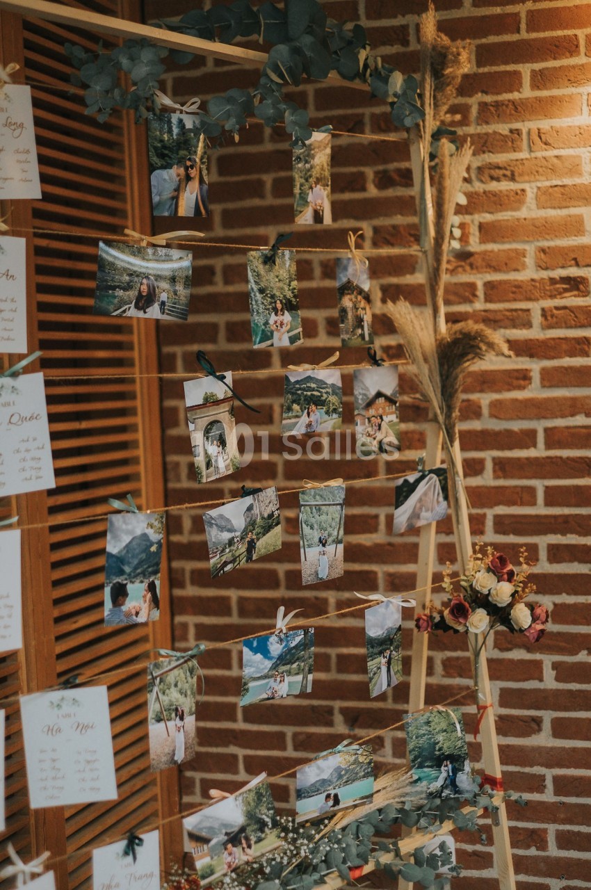 Photos accrochées à une structure en bois décorée de feuillage et de fleurs, devant un mur en briques.