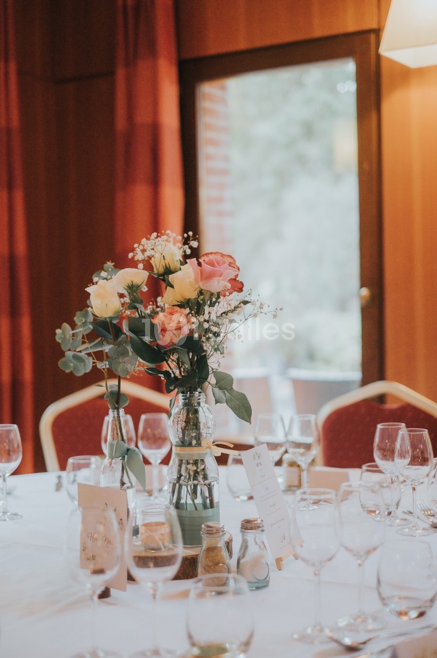 Bouquet de fleurs colorées au centre d'une table dressée avec des verres dans une salle éclairée par la lumière naturelle.