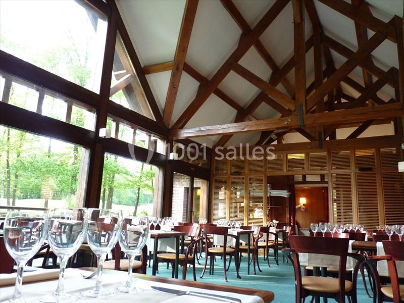 Salle de restaurant lumineuse avec charpente en bois apparent, tables dressées et grandes baies vitrées donnant sur la…