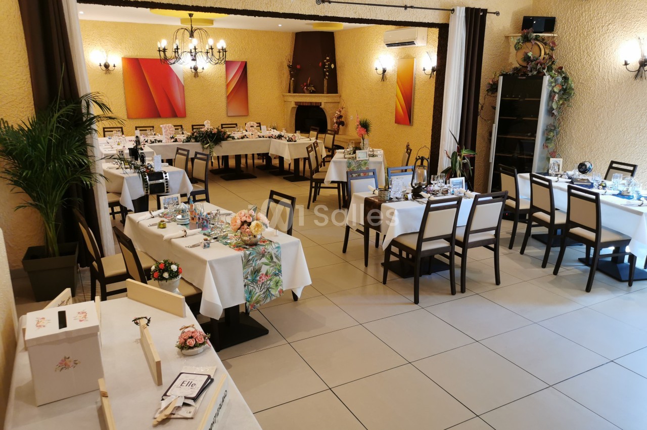 Salle de réception décorée avec des tables dressées pour un événement, ornées de fleurs et d'éléments festifs.
