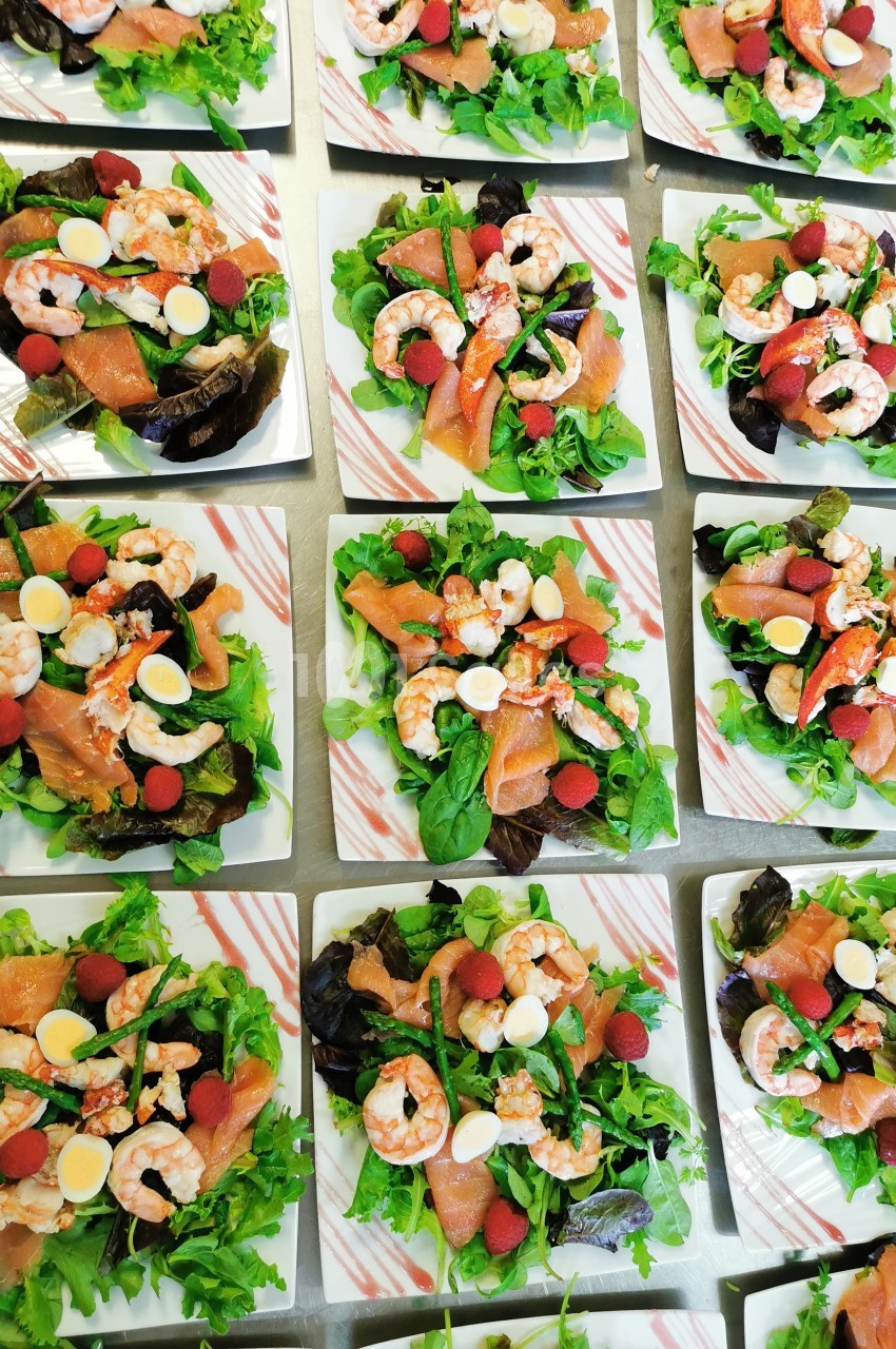 Assiettes de salades composées avec crevettes, saumon fumé, œufs de caille, framboises et feuilles vertes.