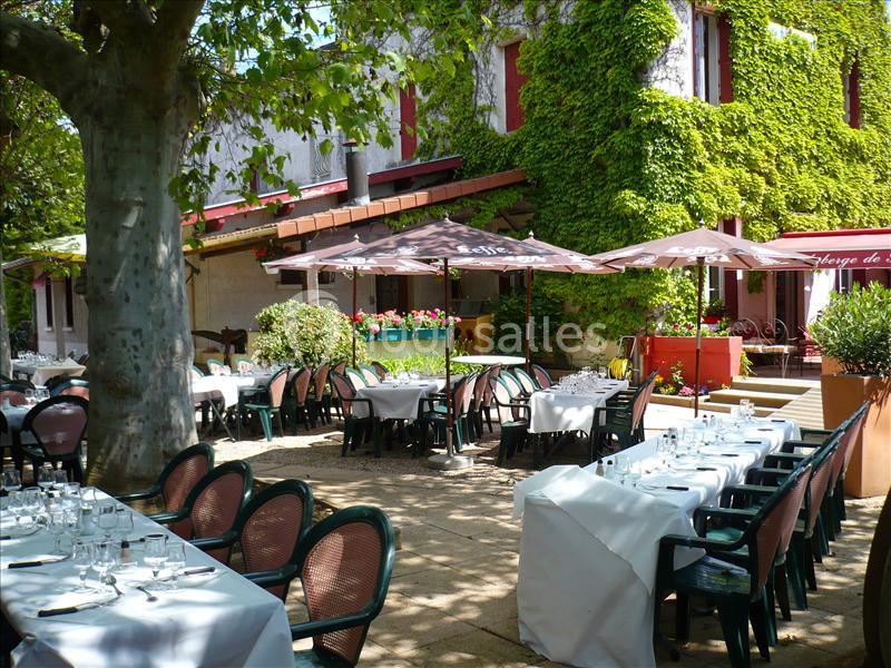 Terrasse d'un restaurant avec des tables dressées, entourée de verdure et ombragée par des arbres et des parasols.