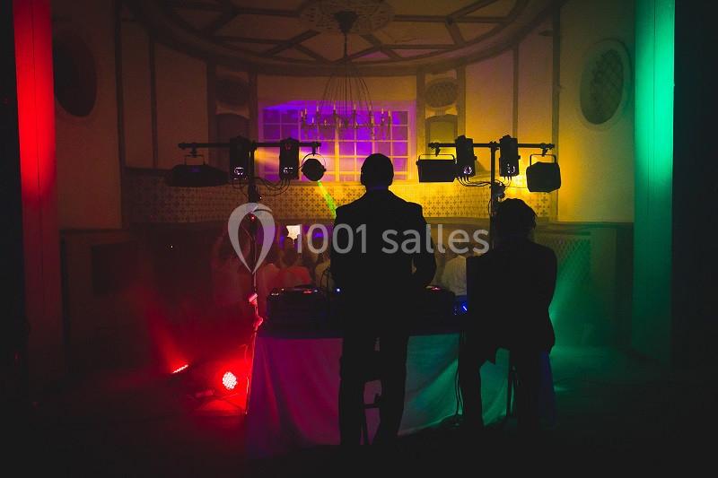 Deux DJ de dos animent une soirée dans une salle éclairée par des lumières colorées.