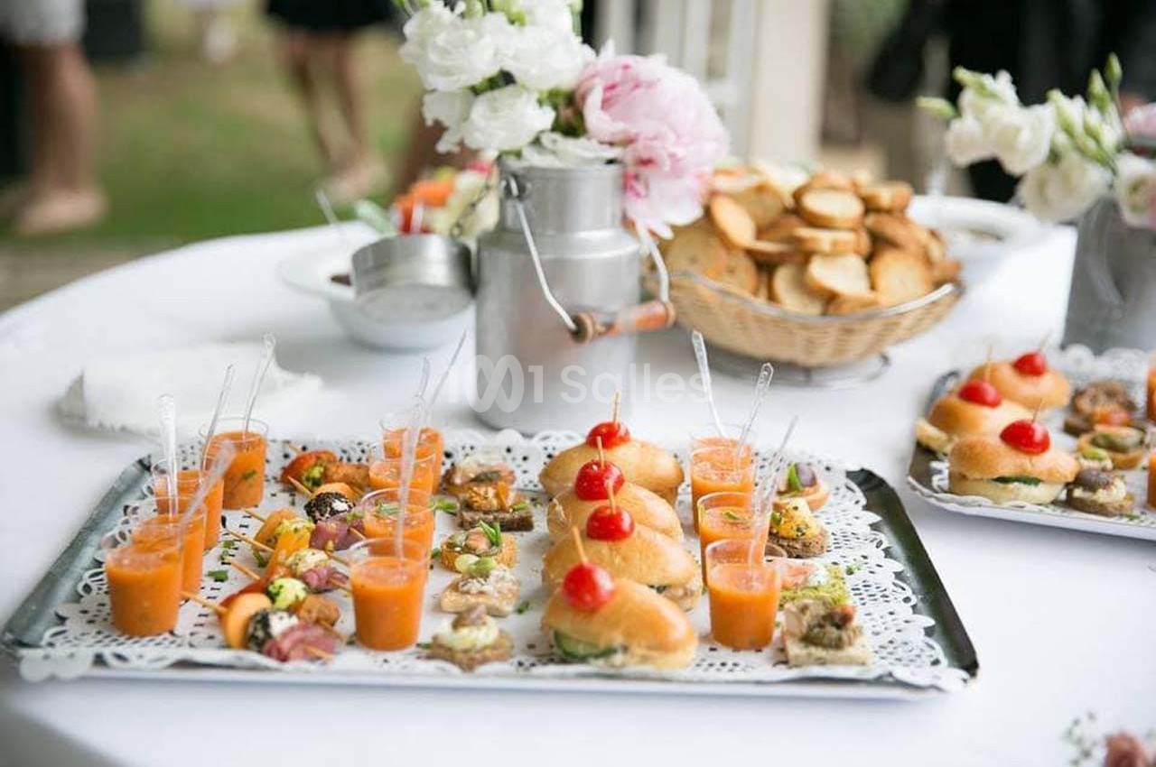 Plateaux de bouchées apéritives variées avec verrines et petits pains, disposés sur une table décorée de fleurs.