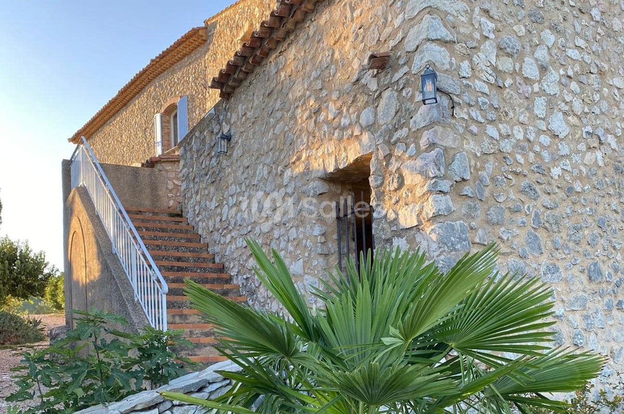 Façade en pierre d'une maison traditionnelle avec escalier extérieur et végétation au premier plan.