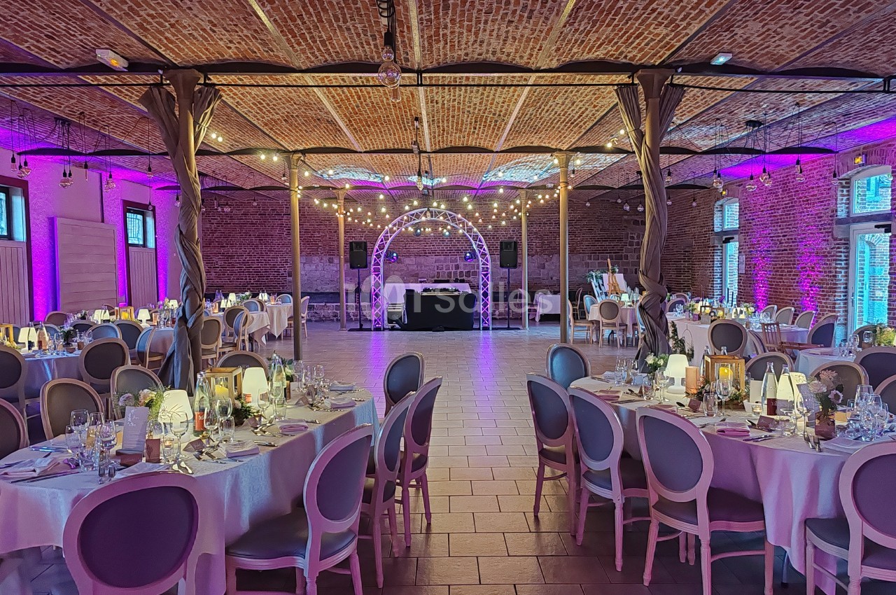Salle de réception décorée avec des tables dressées, éclairage tamisé et guirlandes lumineuses suspendues.