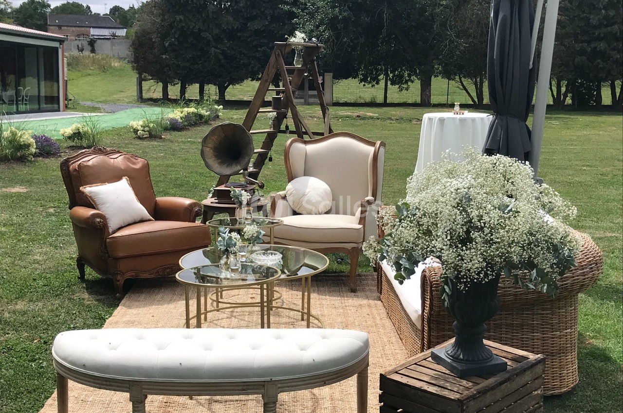 Mobilier vintage disposé en extérieur avec fauteuils, table basse, gramophone et décoration florale sur pelouse.