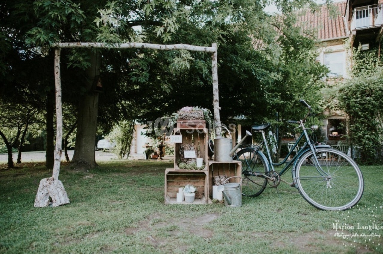 Un vélo ancien posé près de caisses en bois et d'objets décoratifs dans un jardin verdoyant.