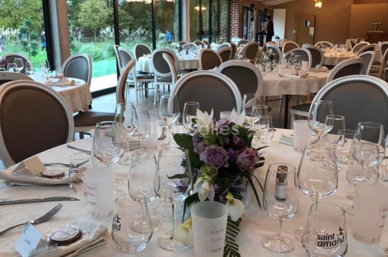 Salle de réception élégante avec tables dressées, décor floral et grandes baies vitrées donnant sur un jardin.