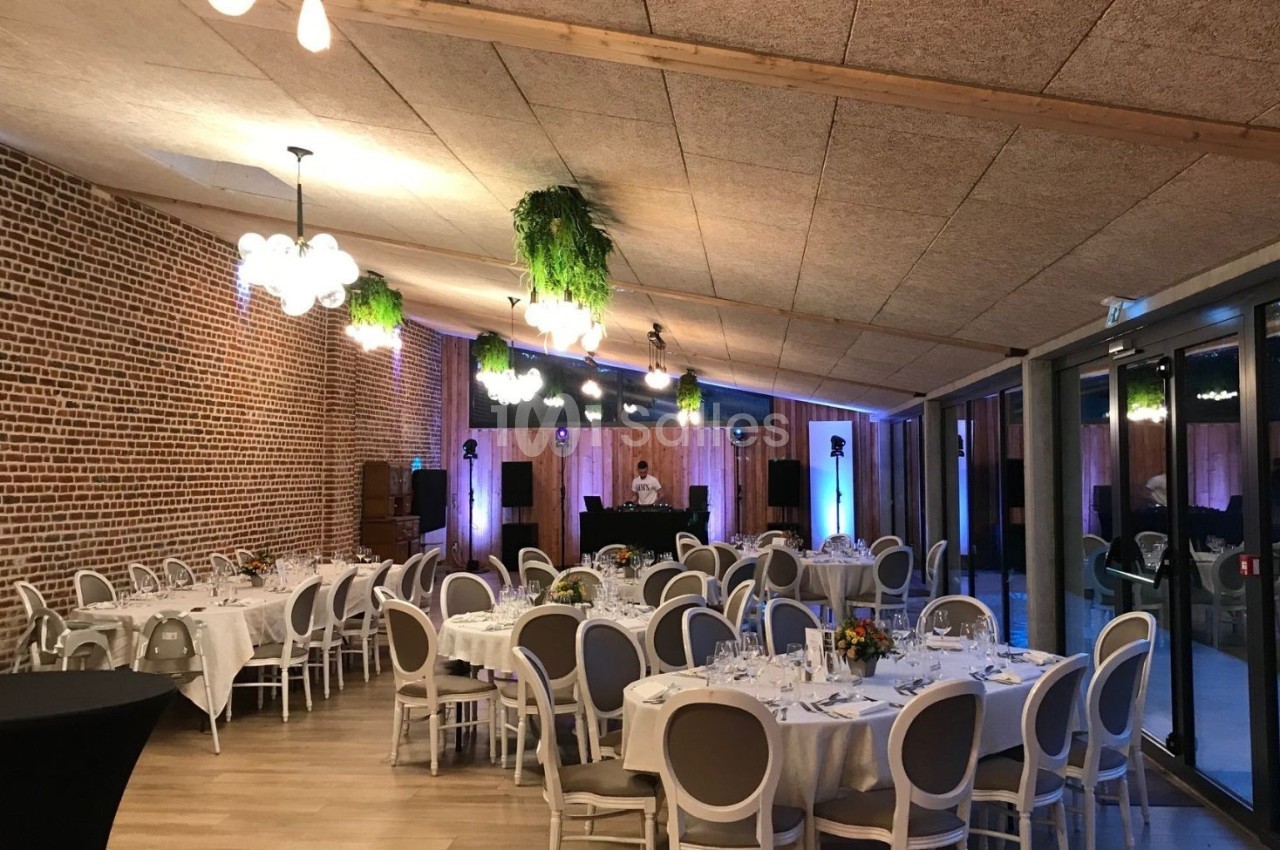 Salle de réception décorée avec des tables dressées, des chaises blanches et des suspensions végétales.