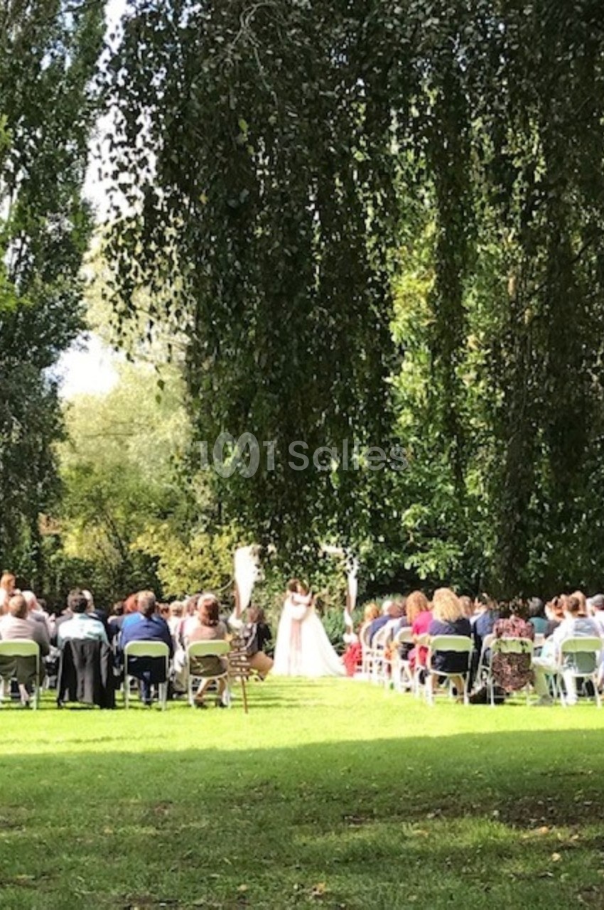 Cérémonie de mariage en plein air avec des invités assis sur des chaises, entourés de verdure et d'arbres.