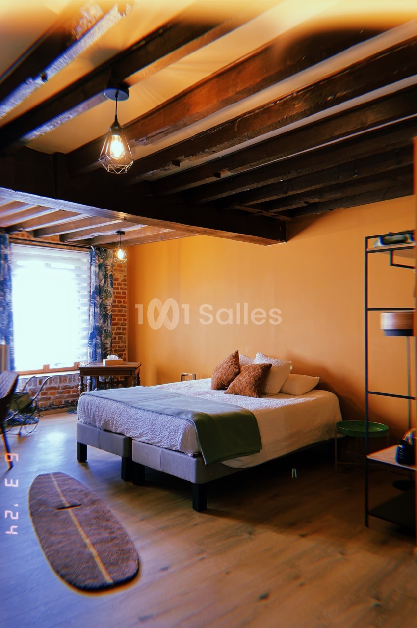 Chambre avec lit double, poutres apparentes, mur orange, bureau près d'une fenêtre et décoration minimaliste.