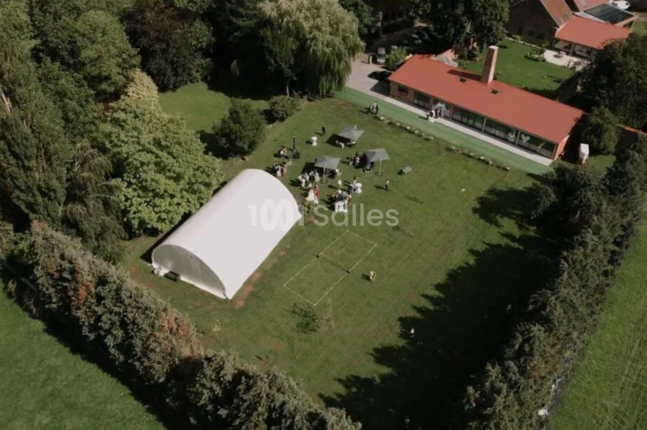 Vue aérienne d'un jardin avec une tente blanche, des tables, des chaises et une maison en arrière-plan.