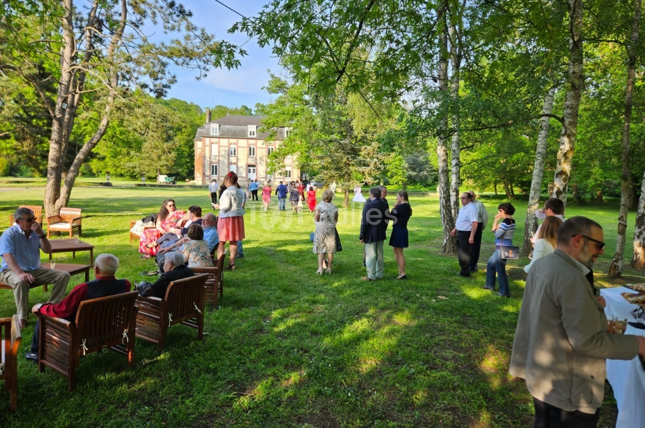 Personnes rassemblées dans un parc verdoyant près d'un bâtiment, discutant ou profitant de l'extérieur.