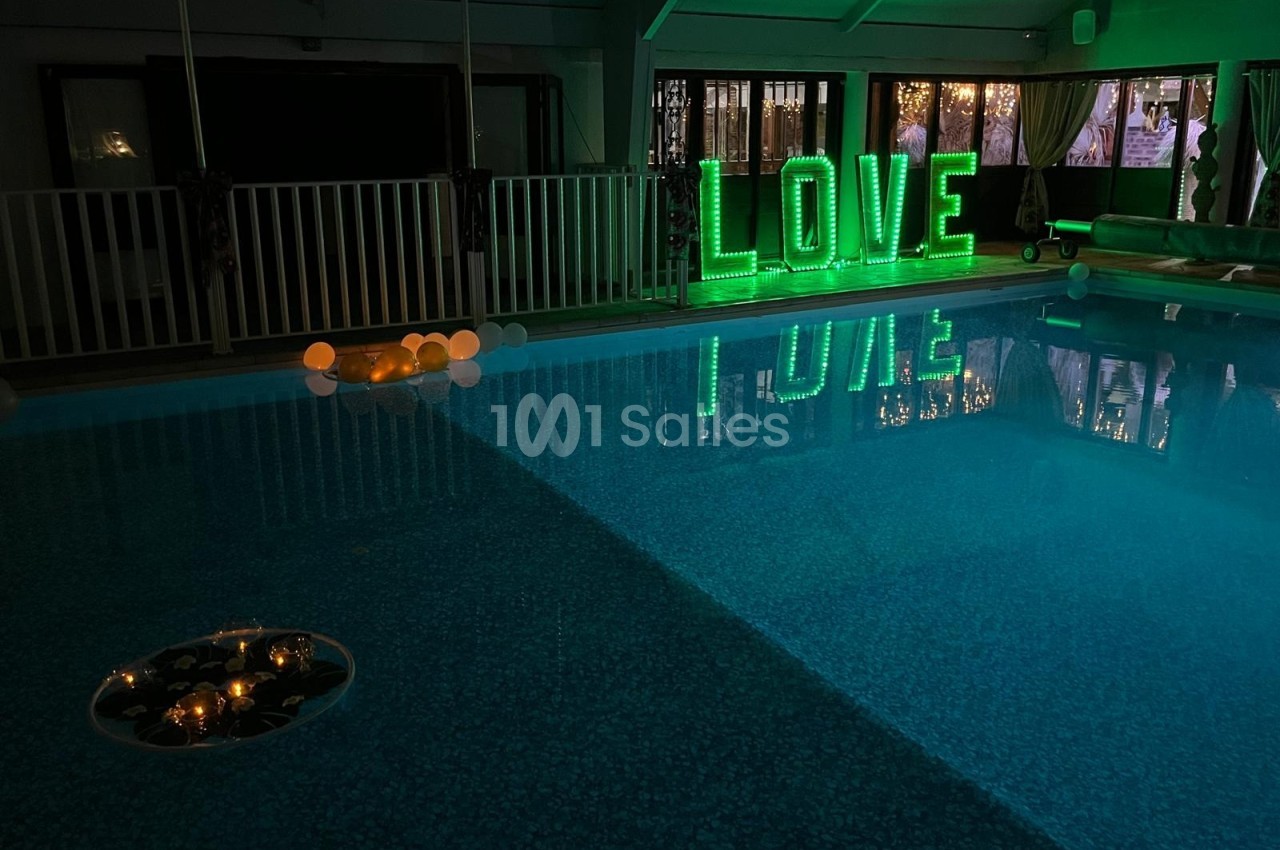 Piscine intérieure éclairée avec des lettres lumineuses vertes formant le mot ’LOVE’ et des bougies flottantes.