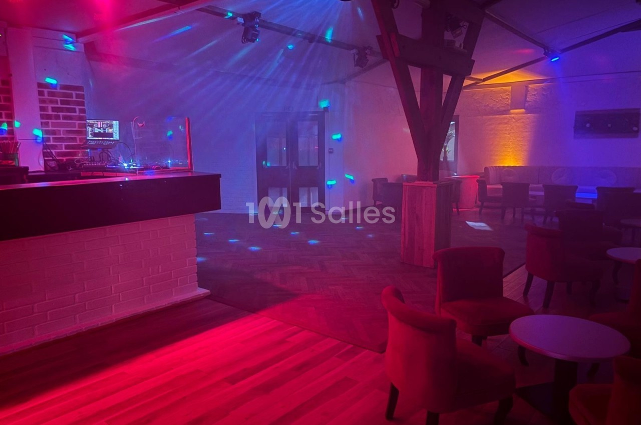 Salle de réception avec éclairage coloré, piste de danse vide, tables et chaises disposées autour.