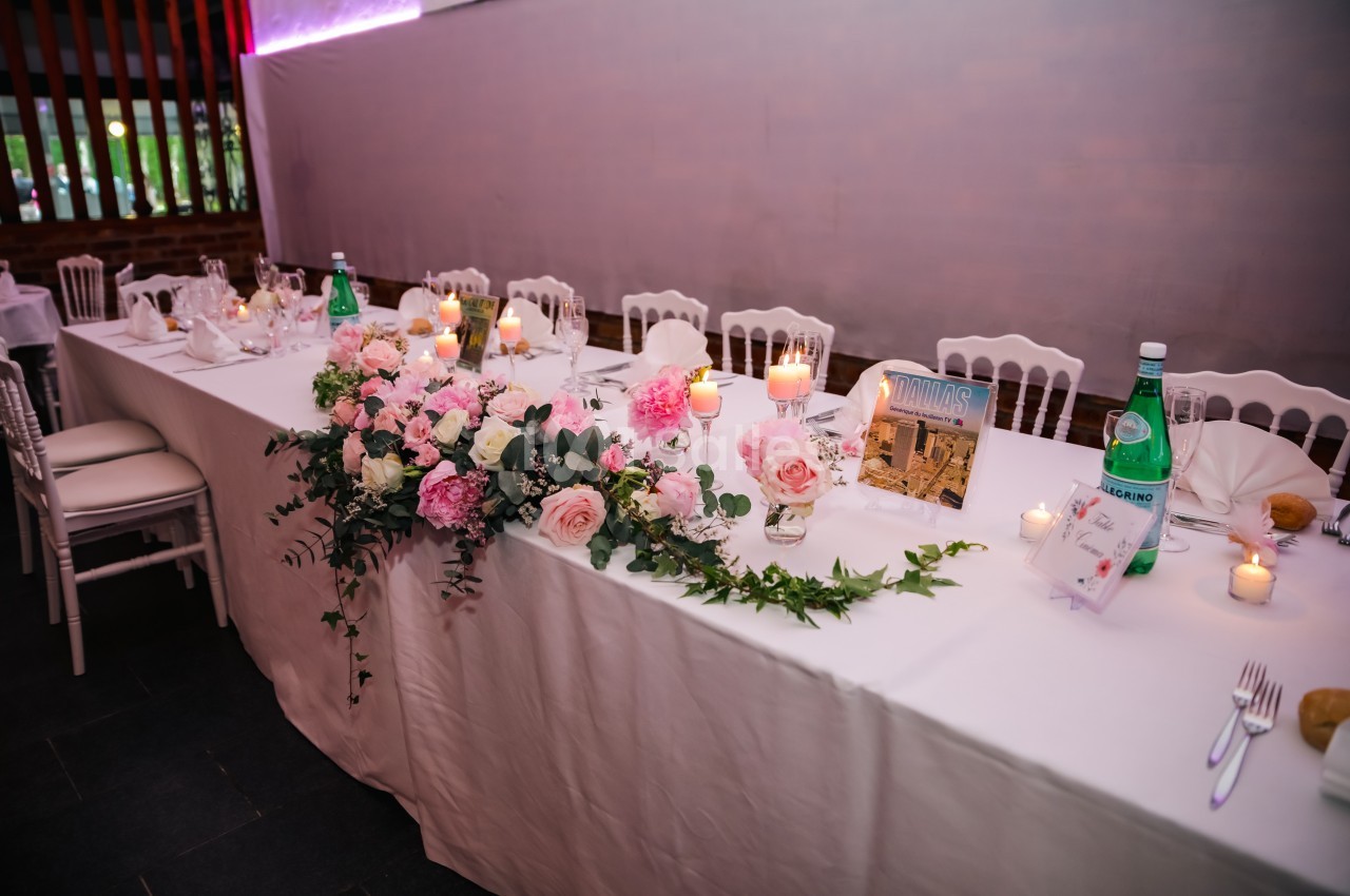 Table de réception décorée de fleurs roses et blanches, bougies allumées et bouteilles d'eau, dans une salle élégante.