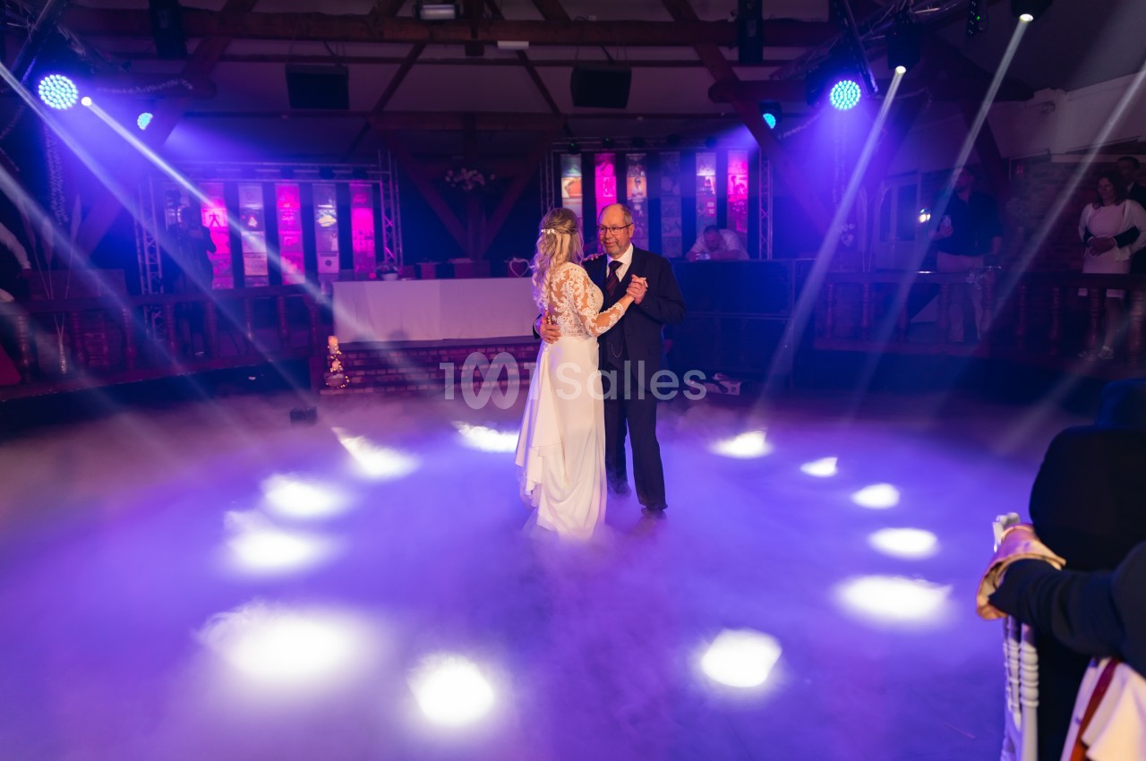 Un couple danse sous des lumières colorées et une ambiance de fumée dans une salle de réception.
