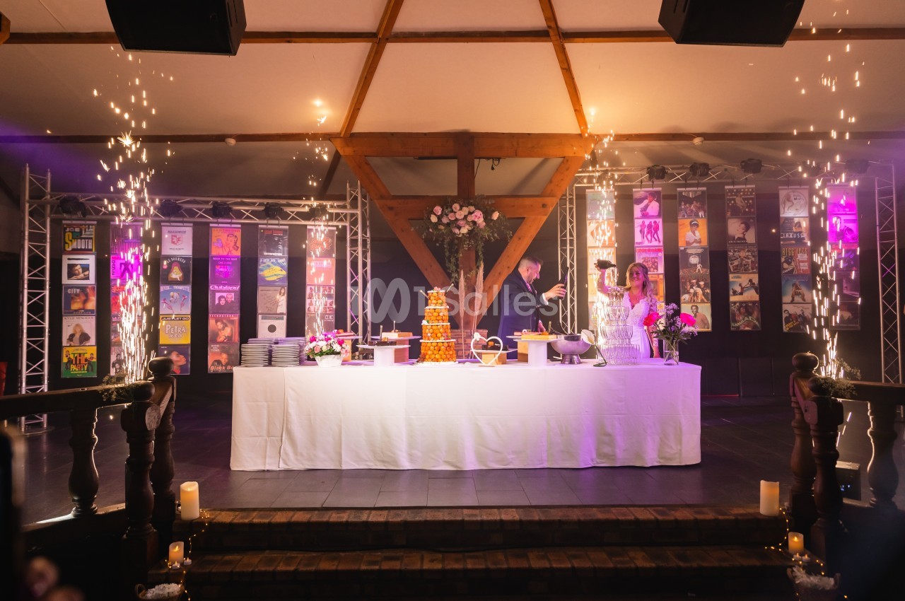 Un couple coupe un gâteau de mariage sur une grande table décorée, entourée de jets d'étincelles et d'éclairages festifs.