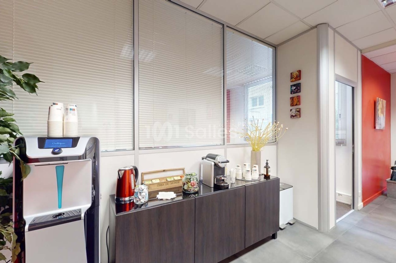 Espace de pause avec machine à café, bouilloire, tasses et décorations sur un meuble dans un bureau lumineux.