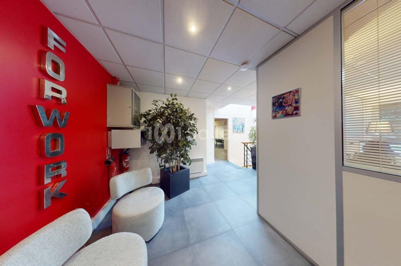Espace d'accueil avec murs rouges, plantes, sièges arrondis et vue sur un couloir lumineux.