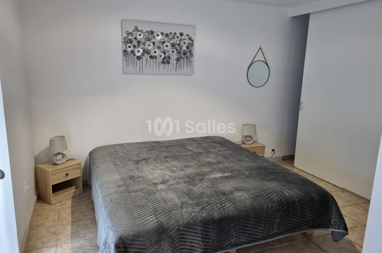 Chambre avec un lit double, couvre-lit gris, tables de chevet en bois, lampes et décoration murale sobre.