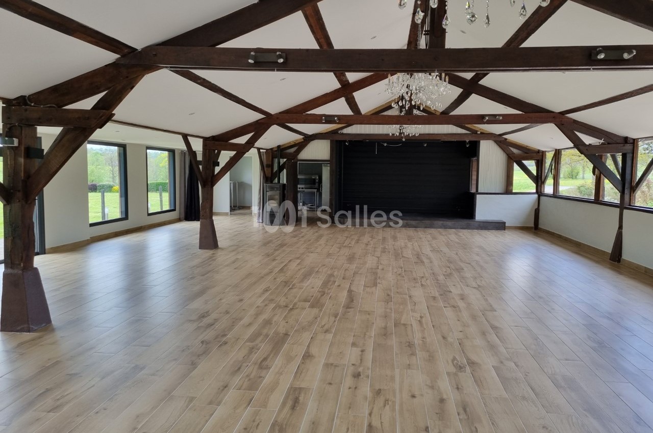 Salle spacieuse avec charpente en bois apparente, parquet clair, scène noire et grandes baies vitrées donnant sur l…