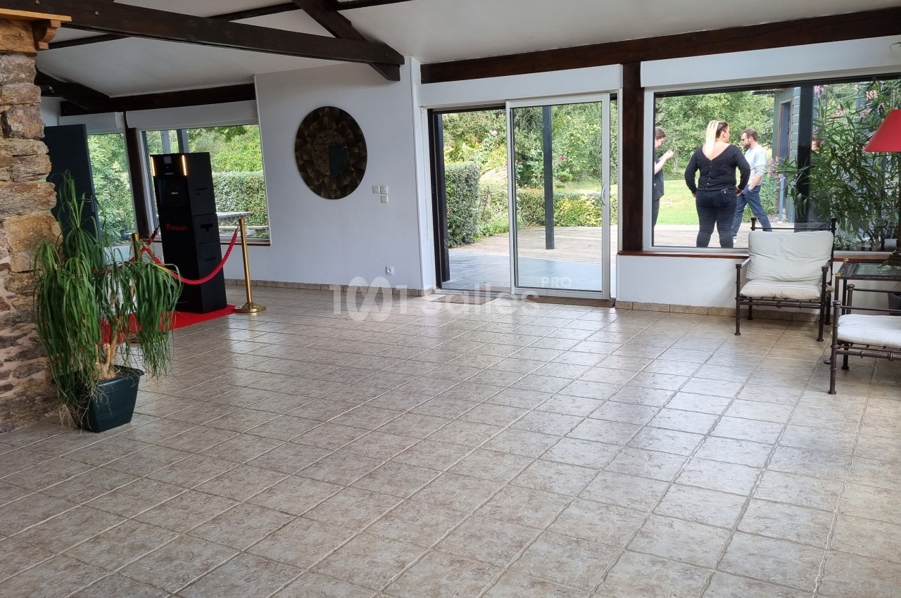 Salle lumineuse avec sol en carrelage, murs en pierre et grandes baies vitrées donnant sur un jardin.