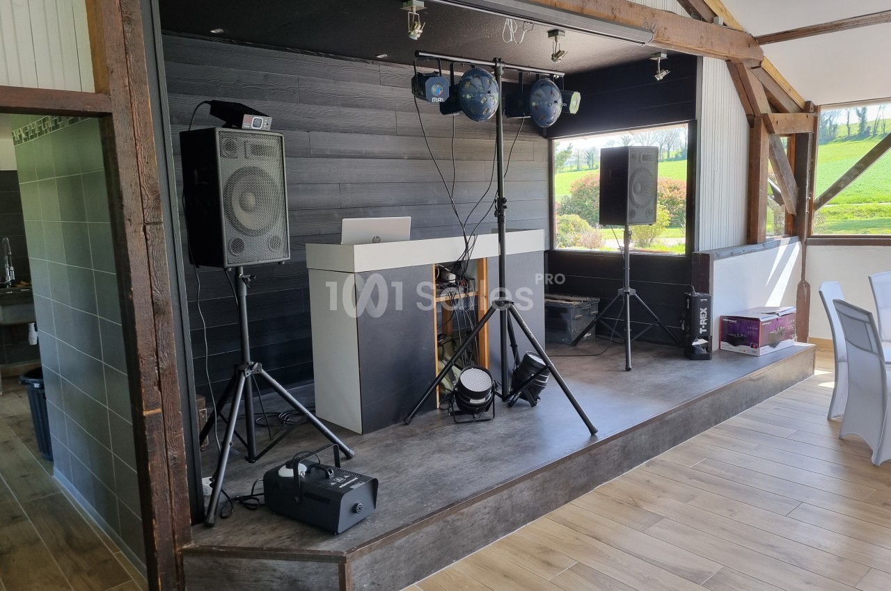 Installation de matériel de sonorisation et éclairage sur une scène en bois dans une salle avec vue sur l'extérieur.