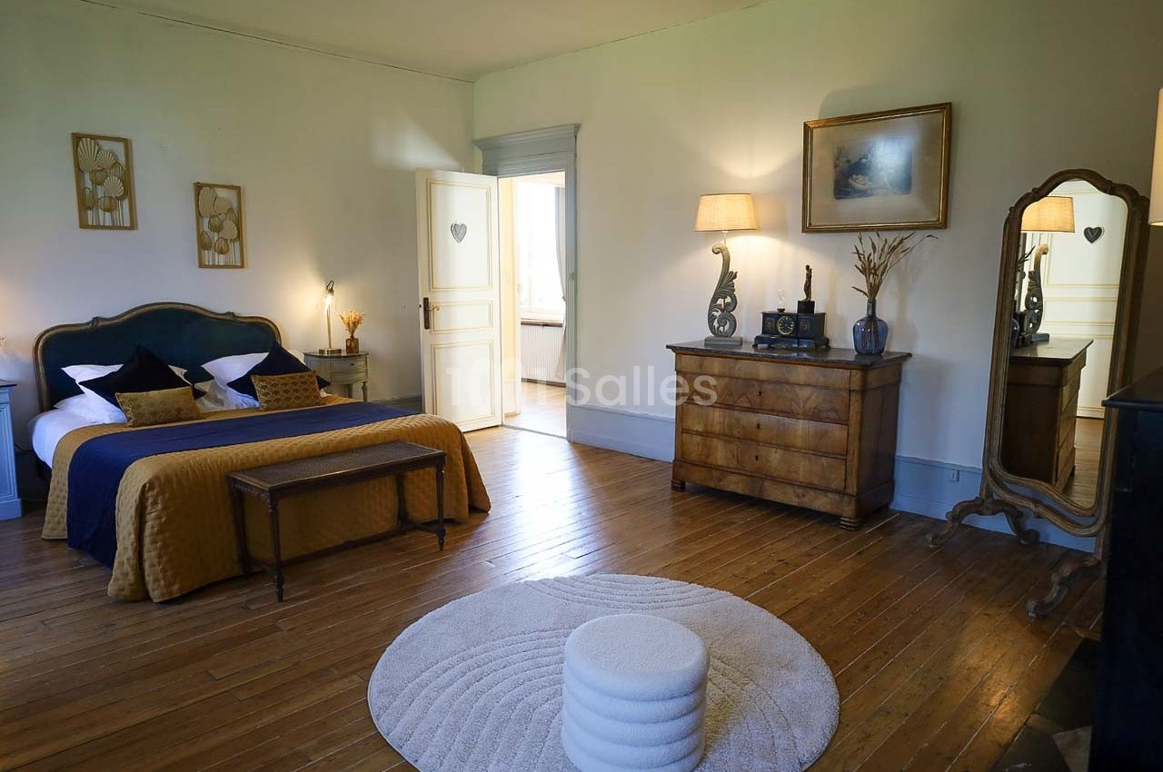 Chambre lumineuse avec lit double, parquet en bois, commode, miroir sur pied et décoration élégante.