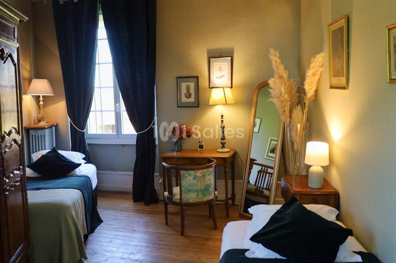 Chambre lumineuse avec deux lits simples, un bureau, un miroir, des décorations murales et des rideaux sombres.