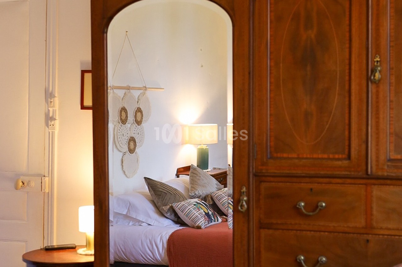 Reflet d'une chambre avec lit, coussins colorés, attrape-rêves au mur et mobilier en bois.