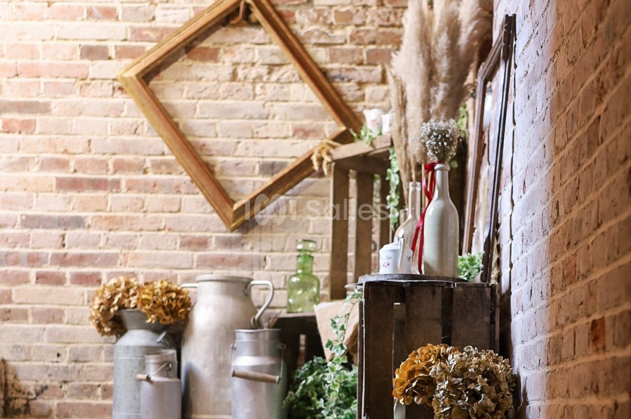 Décoration rustique avec cadres en bois, pots en métal, bouteilles en verre et fleurs séchées sur fond de mur en briques.
