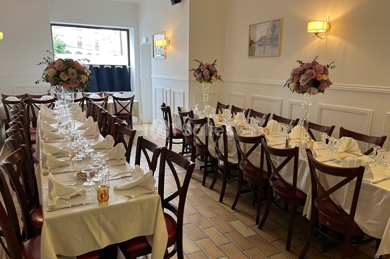 Salle de réception élégamment dressée avec des tables alignées, nappes blanches et bouquets de fleurs roses.