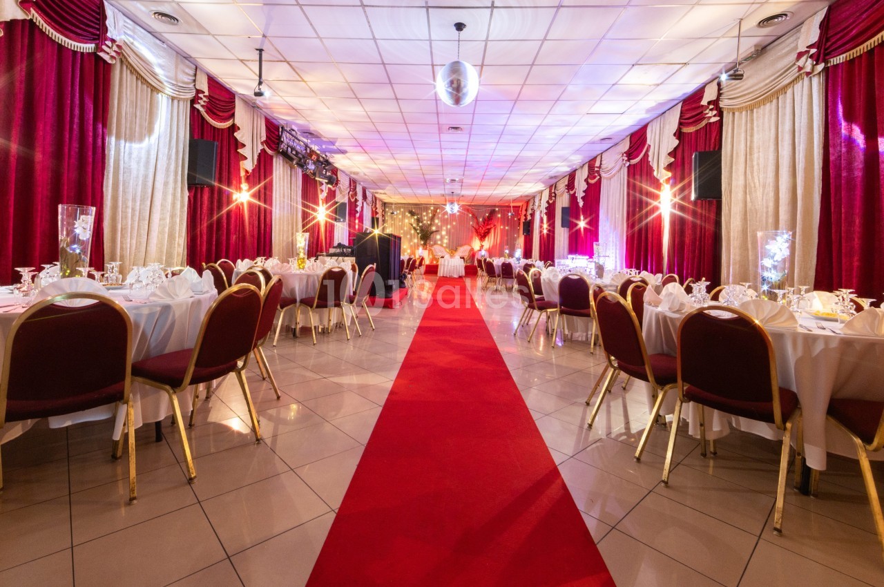 Salle de réception décorée avec des tables dressées, un tapis rouge central et des rideaux rouges et dorés.