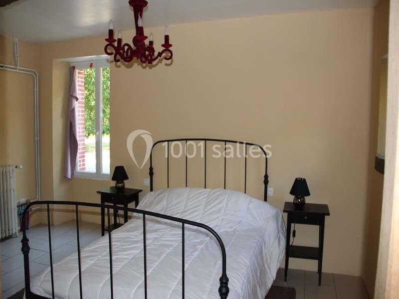 Chambre avec un lit double en métal noir, deux tables de chevet avec lampes et un lustre rouge, éclairée par une fenêtre.