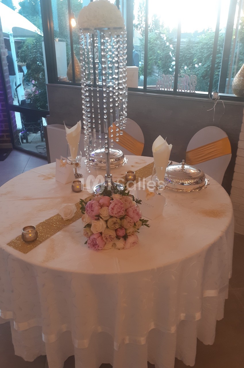 Table décorée pour un événement avec nappes blanches, centre de table floral, chandelles et éléments dorés.