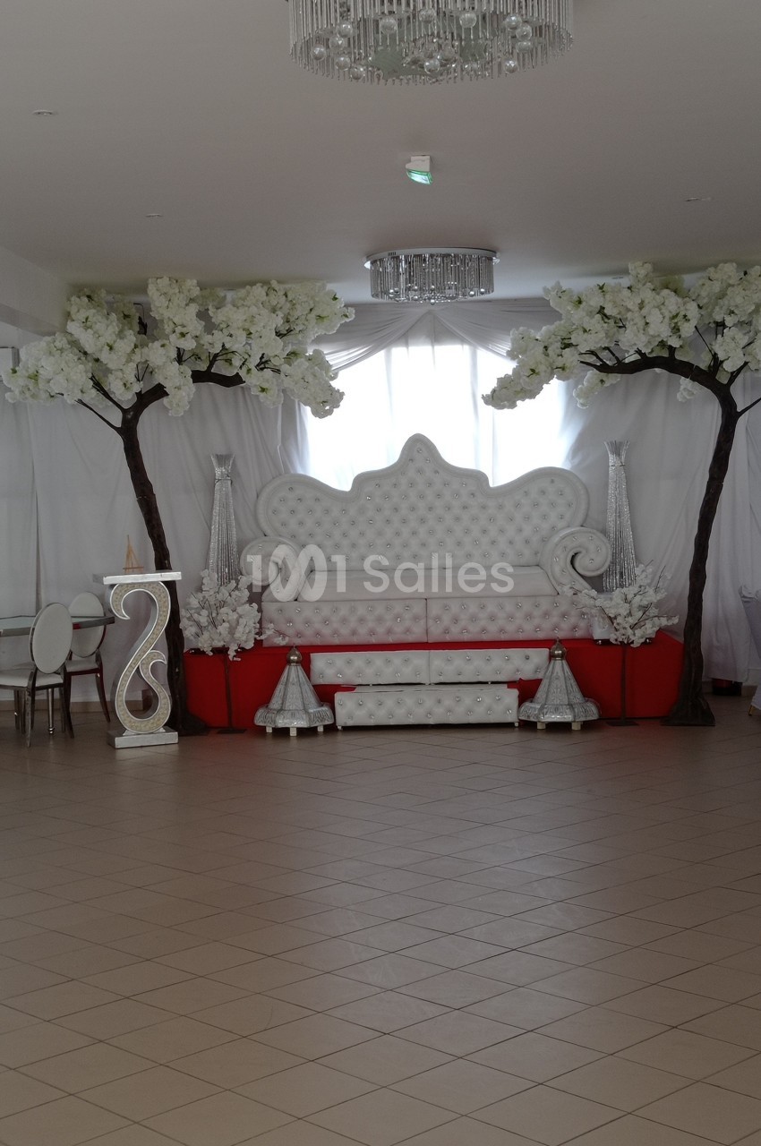 Salle décorée avec un canapé capitonné blanc, des arbres artificiels fleuris et des éléments décoratifs argentés.