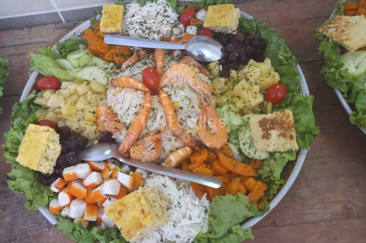 Assiette garnie de crudités, crevettes, morceaux de fromage, légumes variés et salade, présentée sur un lit de laitue.