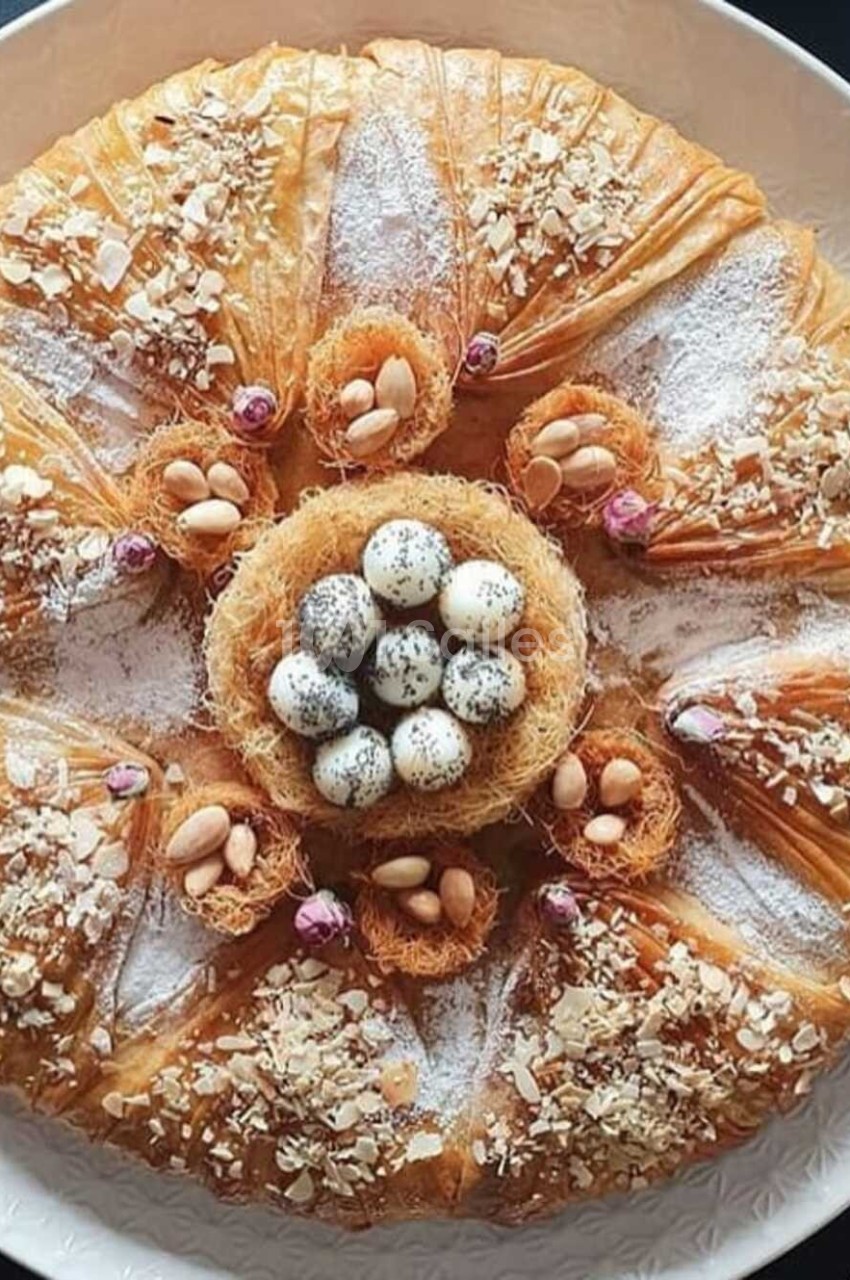 Pâtisserie circulaire en pâte filo garnie de fruits secs, sucre glace et œufs décoratifs au centre.