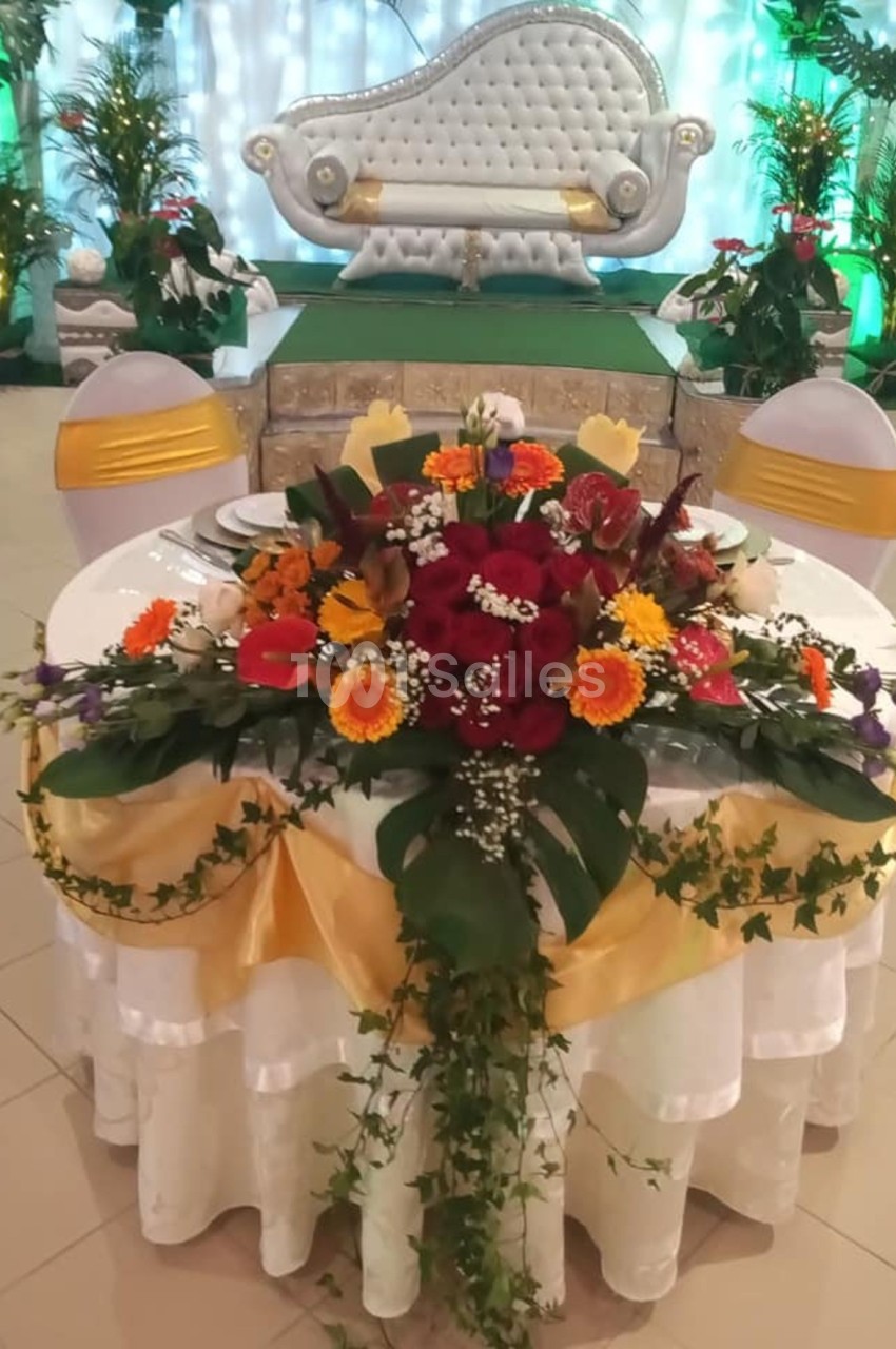 Table décorée avec des fleurs colorées et rubans dorés, devant une estrade ornée d'un canapé blanc capitonné.