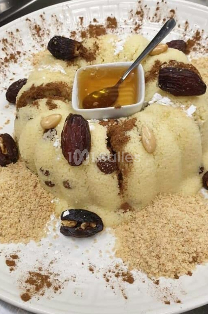 Assiette de semoule garnie de dattes, amandes, cannelle, miel au centre et poudre de biscuit autour.