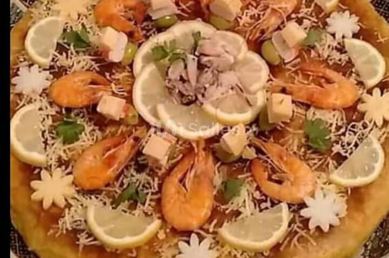 Grande galette garnie de crevettes, rondelles de citron, fromage, olives et décorations florales comestibles.
