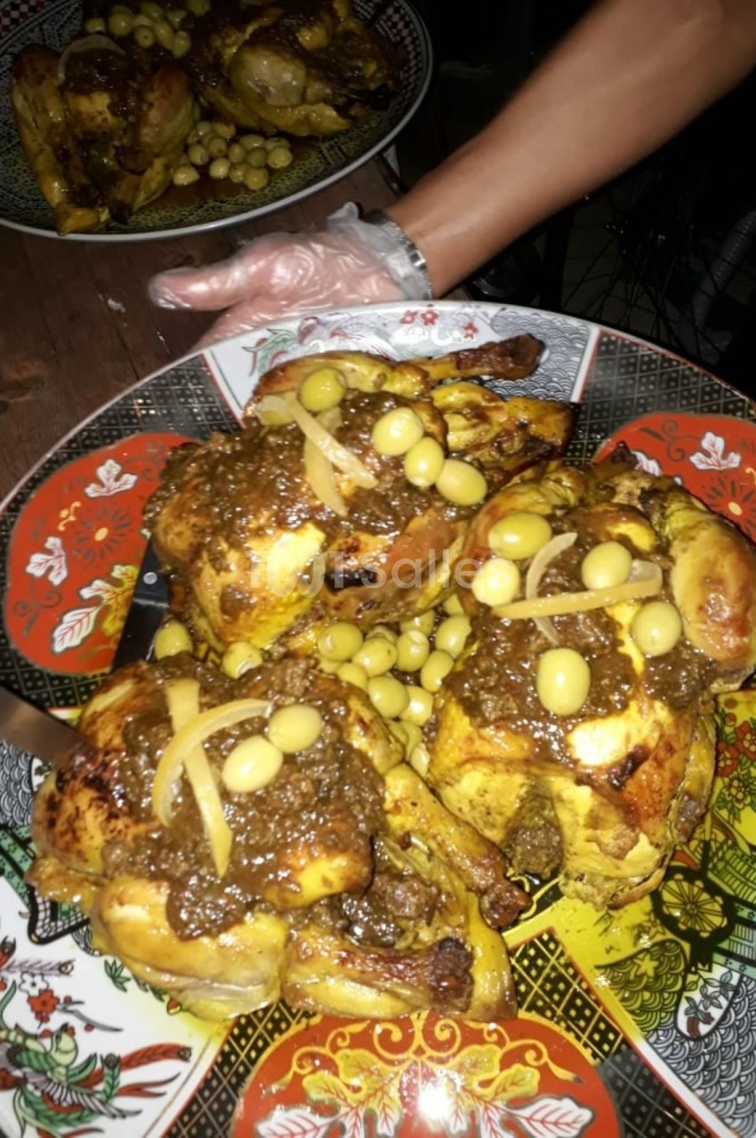 Poulet rôti garni d'olives et d'oignons, nappé de sauce épicée, présenté sur un plat décoratif.