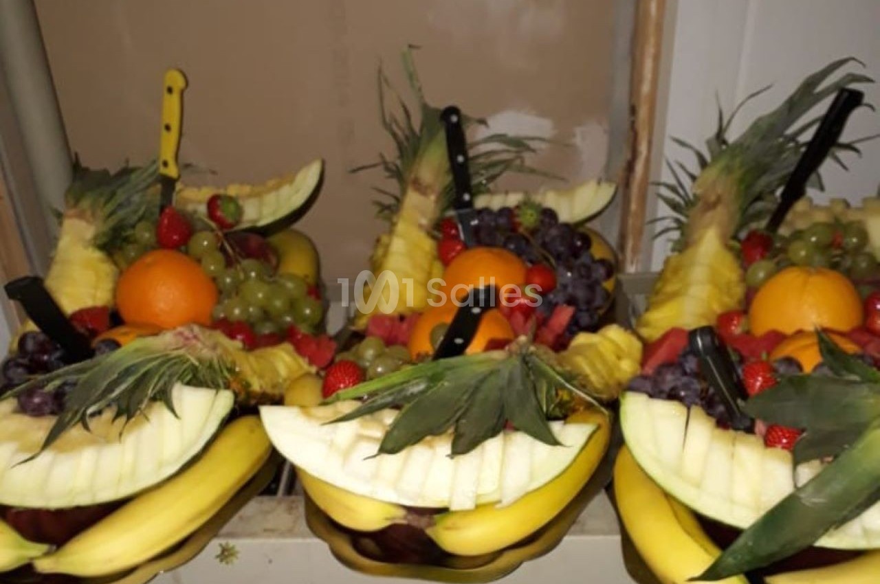 Plateaux de fruits frais composés de bananes, ananas, raisins, fraises, oranges et pastèques, décorés avec des couteaux.