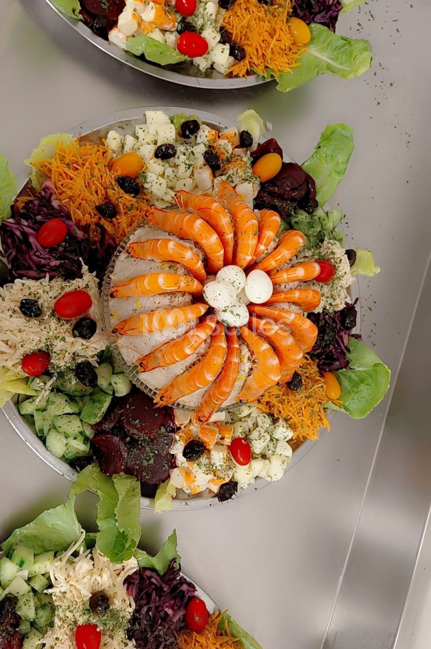 Assiette garnie de crevettes, légumes variés, œufs et olives, présentée avec soin sur un lit de salade.