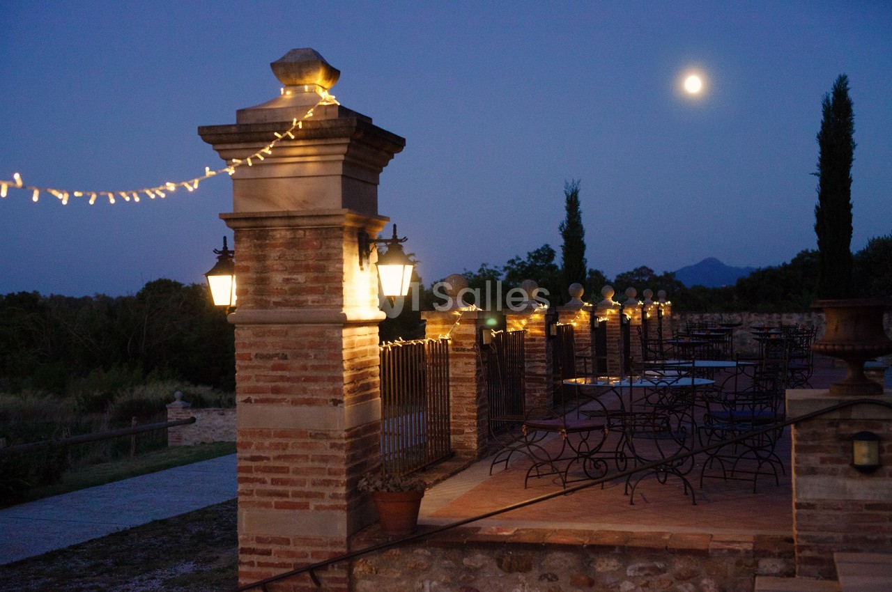 Terrasse éclairée par des guirlandes lumineuses et des lampadaires, avec vue sur un paysage nocturne sous la pleine lune.